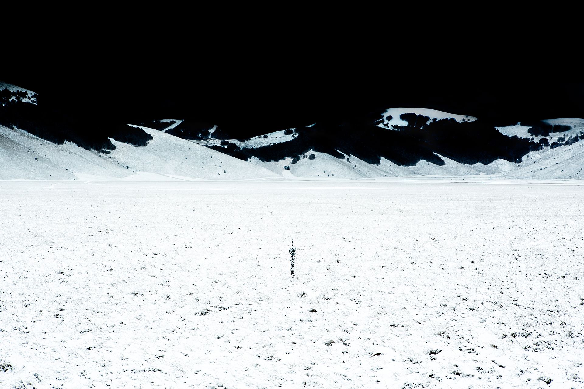 Distesa di neve con un palo solitario al centro e le montagne scure all'orizzonte