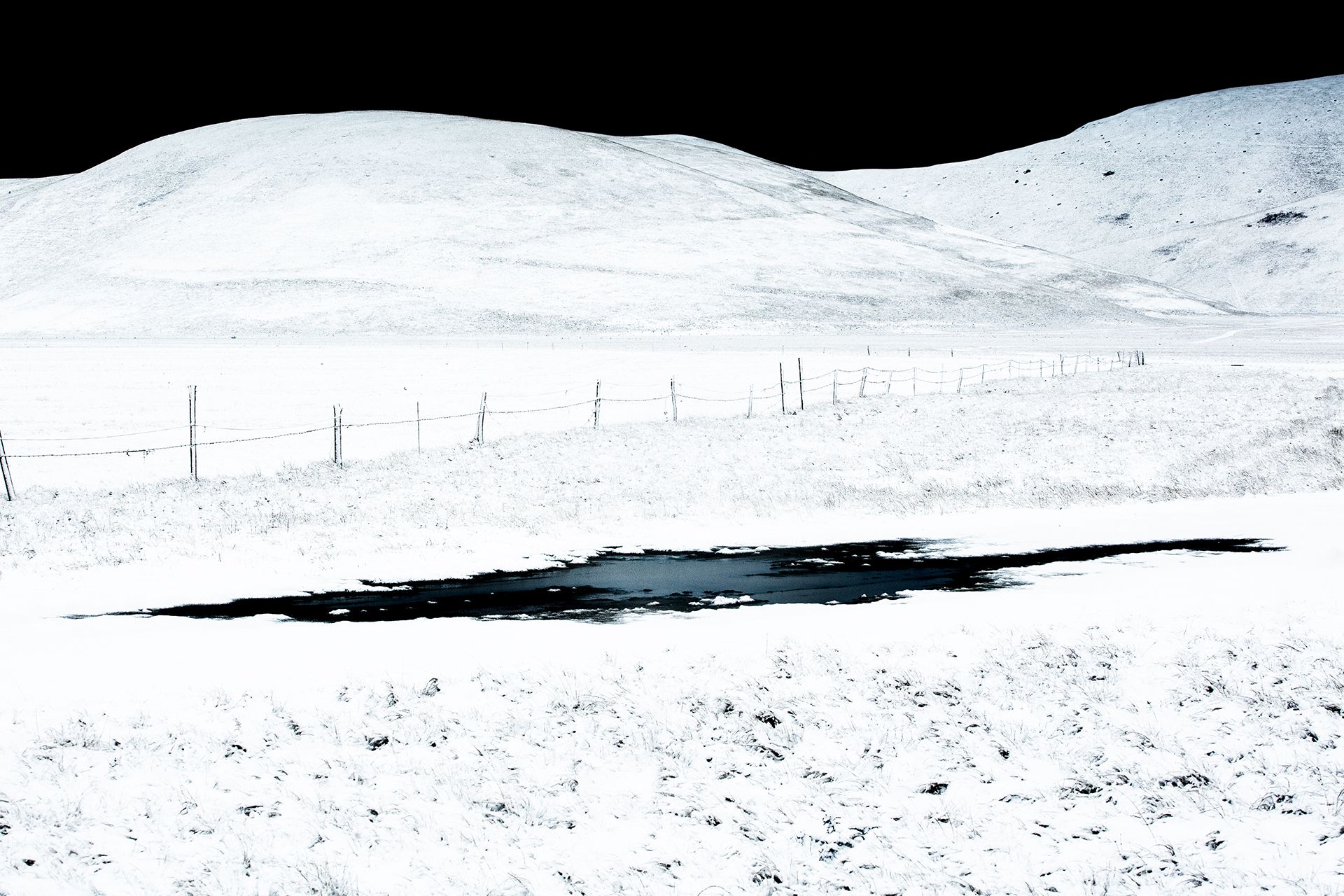 Piana di Castelluccio innevata con una staccionata e una pozza d'acqua scura in primo piano