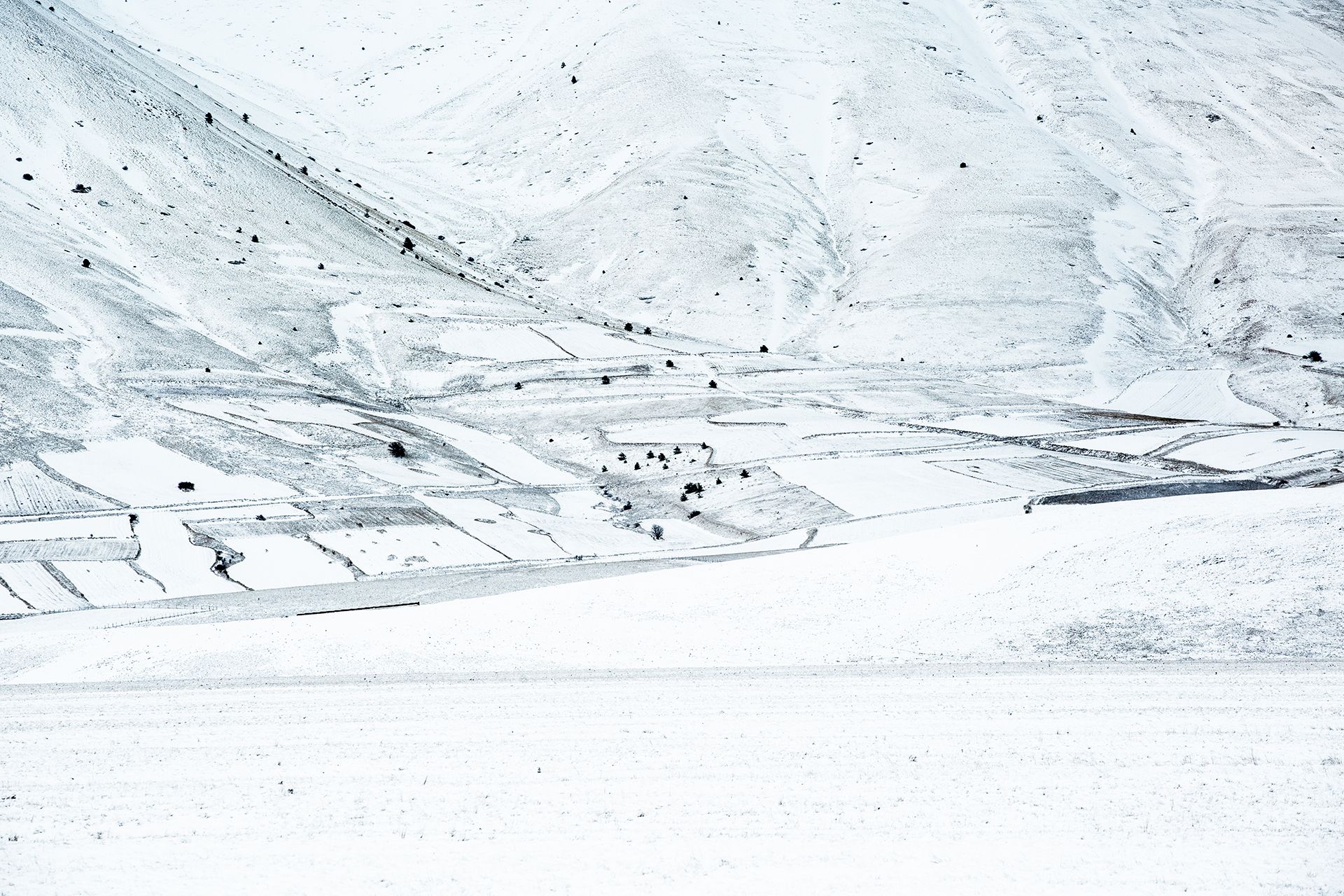 Versante di montagna innevato solcato da sentieri e piccoli terrazzamenti