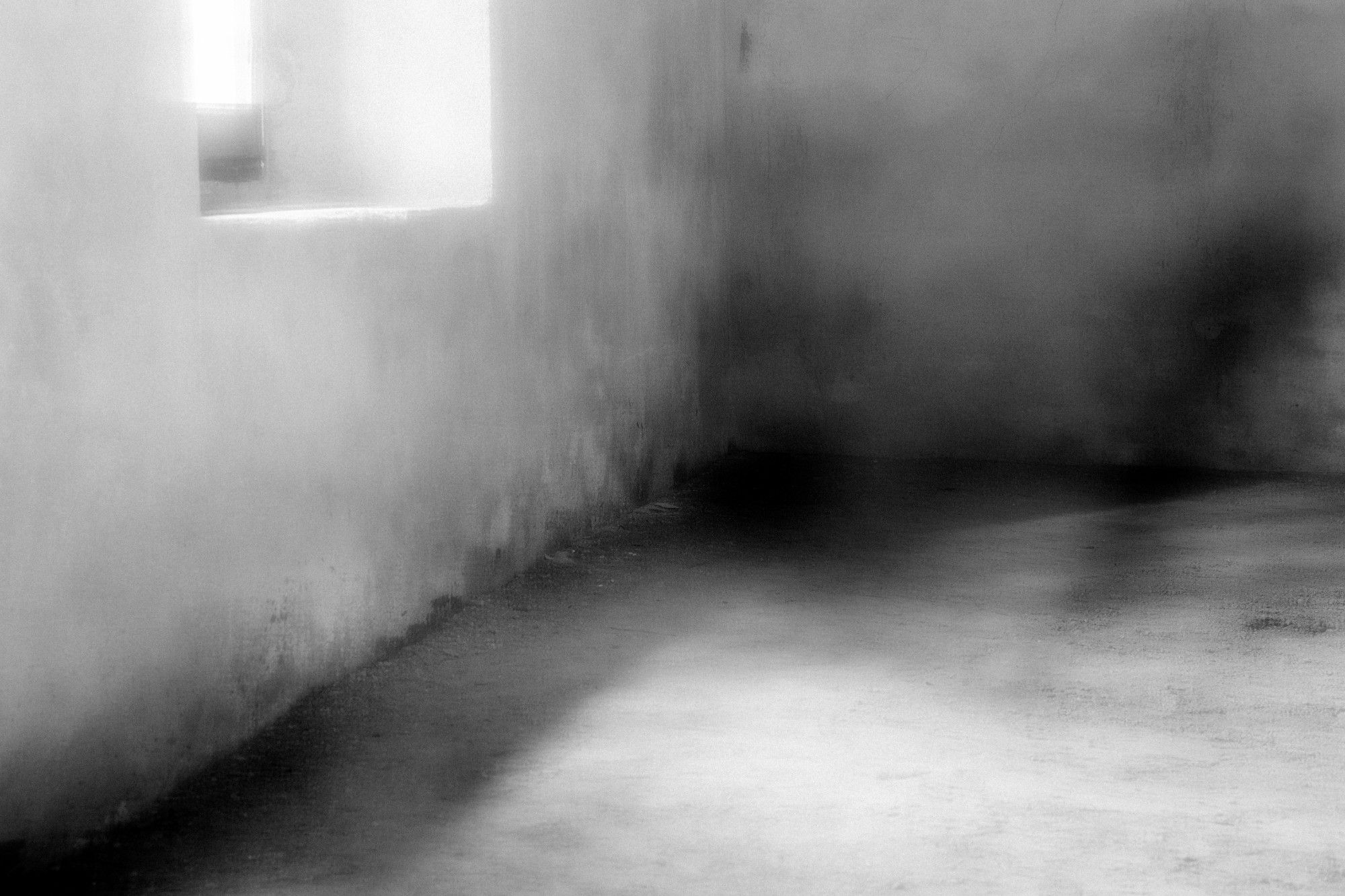 Parete bianca sfocata con una finestra di luce e ombre sul pavimento in cemento