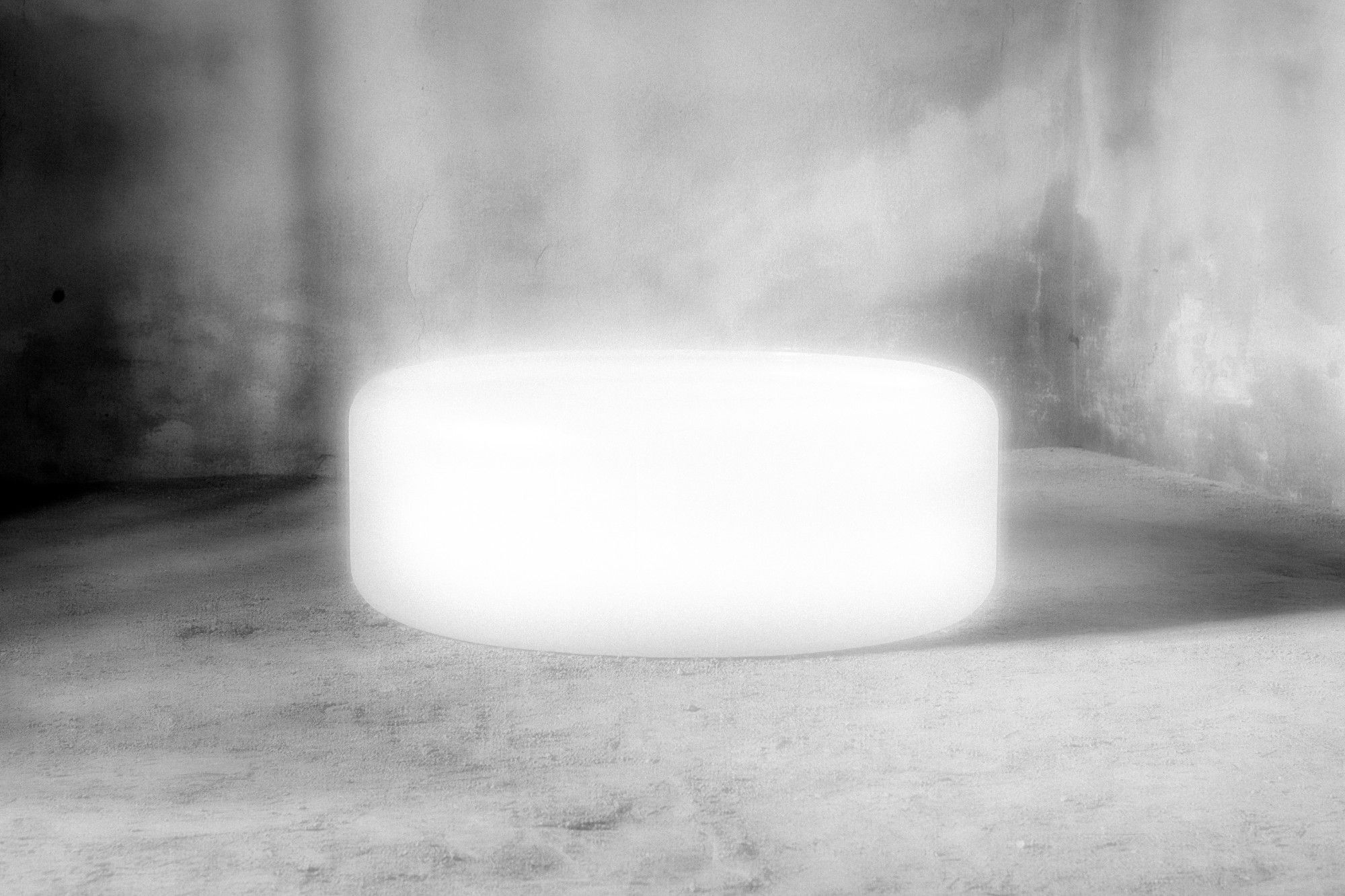 Cilindro bianco luminoso al centro di una stanza in cemento