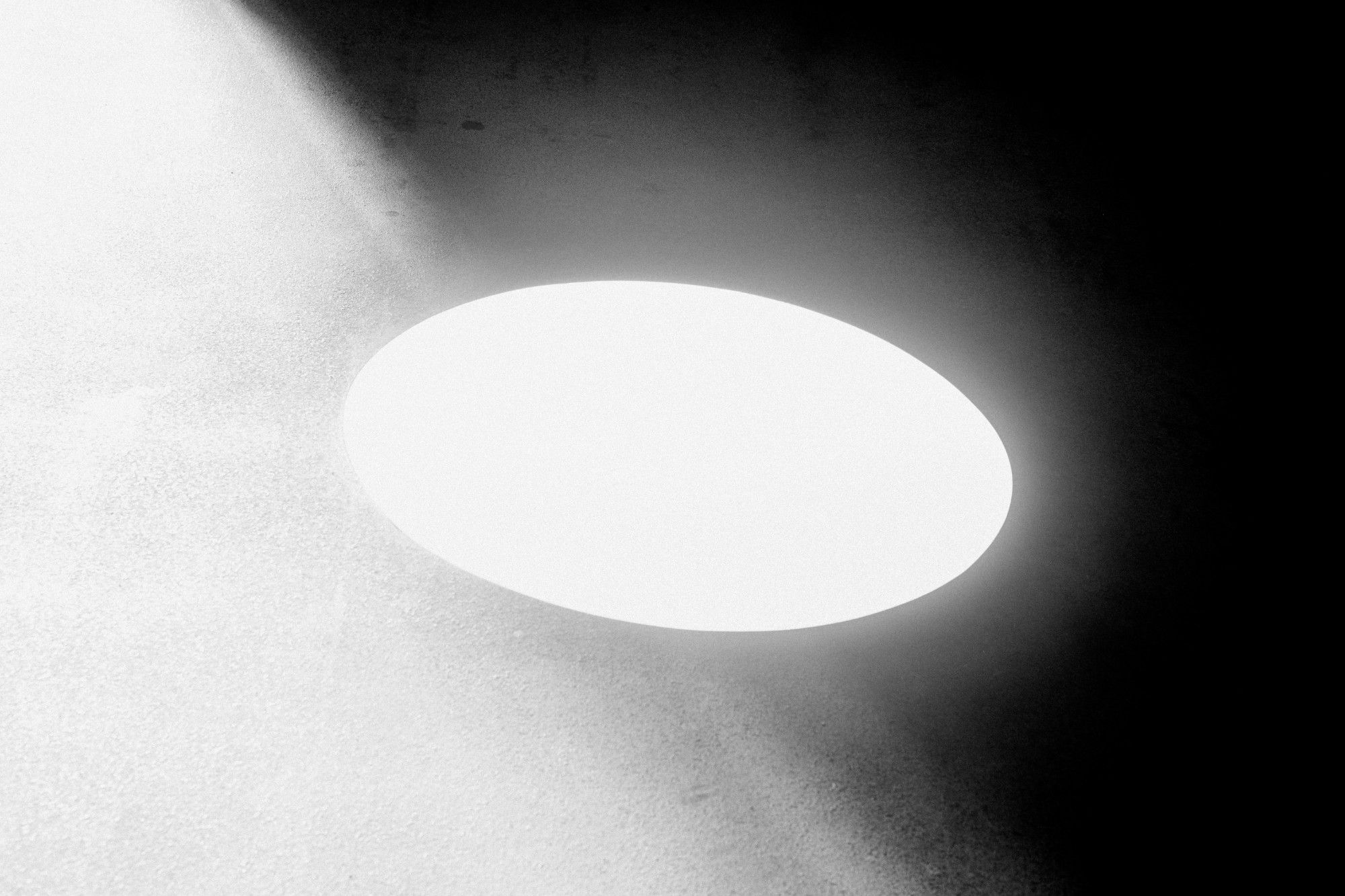 Ellisse bianca di luce su una superficie in cemento, con l'ombra a destra
