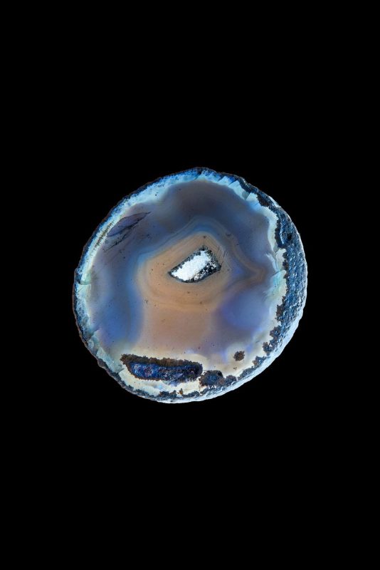 Fetta circolare di agata con anelli concentrici grigi e azzurri su fondo nero